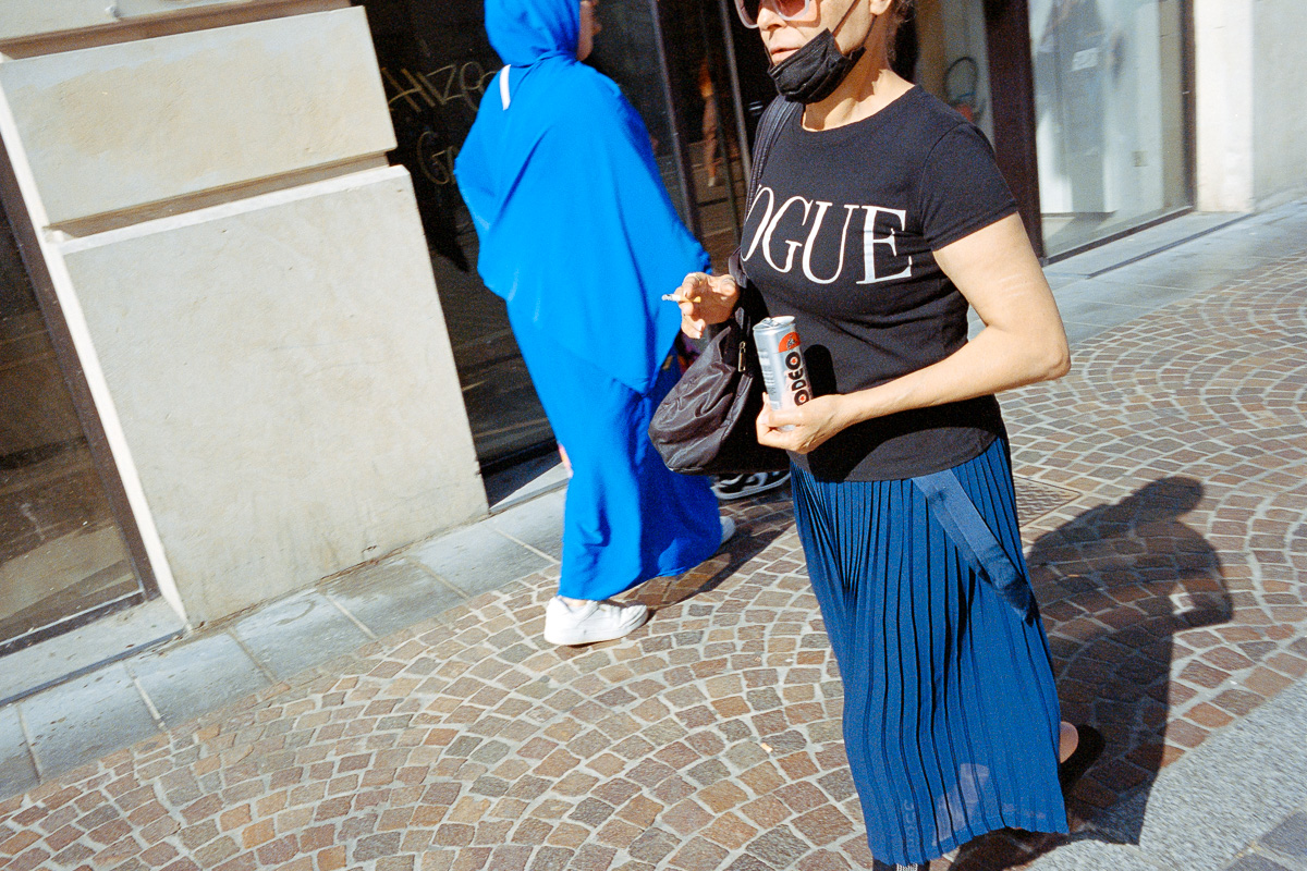 Une femme marche dans la rue avec un tee-shirt Vogue, une cigarette et un canette de soda à la main